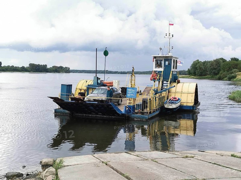 A small ferry sails on a quiet river, Vistula, under a cloudy sky, Poland