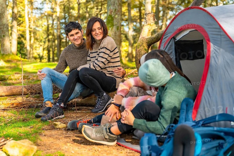Family talking relaxed sitting on camping tent in an alpine forest enjoying weekend together