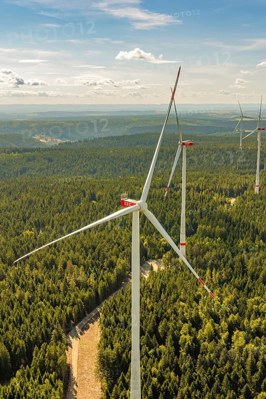 A towering wind turbine stands in a large, densely wooded area under a blue sky, Besenfeld, Freudenstadt district, Germany