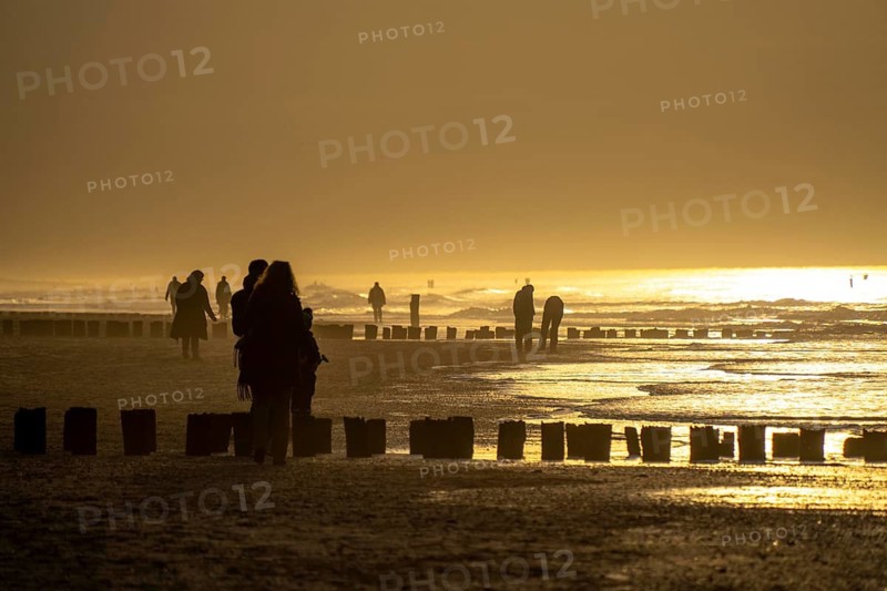 Winter on the North Sea, sunset at sea, beach walkers, coastal protection, through wooden posts, paalhoofden, on the beach, breakwater, the piles rammed into the sandy soil in double rows slow down the waves and ocean currents and thus slow down the flow rate of seawater, so less sand is washed away from the standing position, near Domburg, Walcheren peninsula in the Dutch province of Zeeland