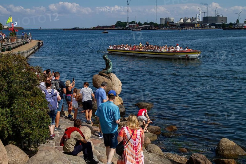 Touristen besuchen die kleine Meerjungfrau-Statue an der Uferpromenade, während ein Boot vorbeifährt, Kopenhagen, Dänemark