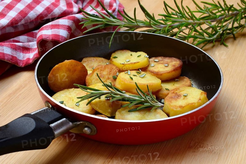 Fried potatoes in pan with rosemary sprig
