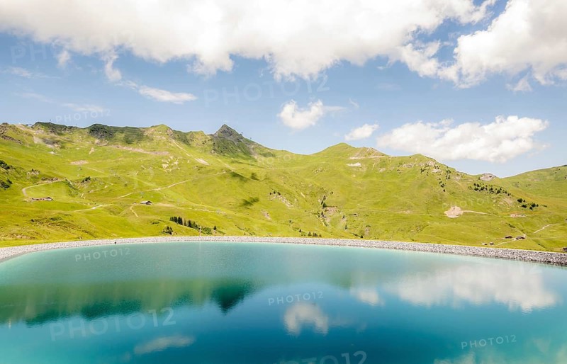 Picturesque view of a tranquil lake reflecting the surrounding green hills of the Swiss Alps, showcasing the natural beauty of Switzerland