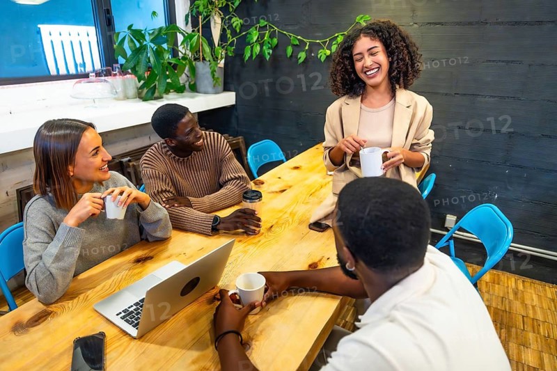 Diverse males and females coworkers smiling and chatting in the canteen of a modern coworking