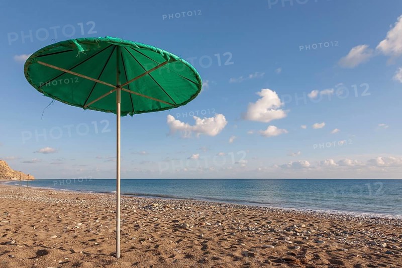 A green parasol stands on a sandy beach under a blue sky with a few clouds, Avdimou Beach, Cyprus