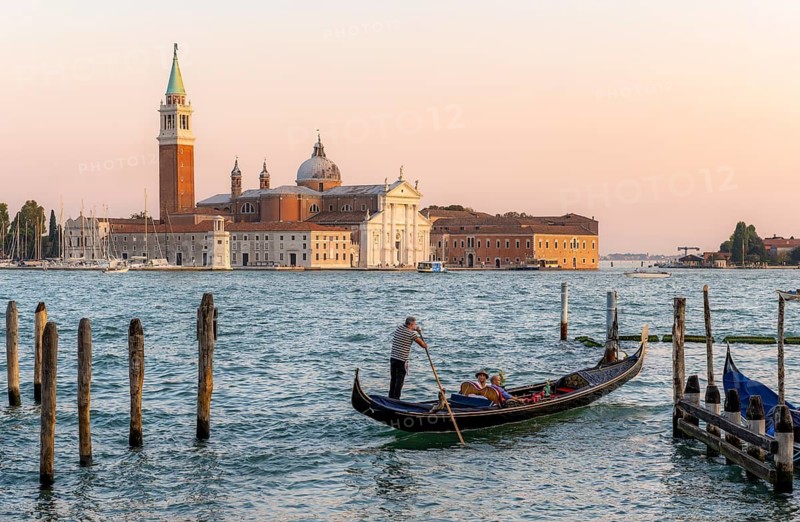 Gondolier with Venetian gondola on the lagoon, in the back island of Isola di San Giorgio Maggiore with church of San Giorgio Maggiore in the evening light, Venice, Veneto, Italy