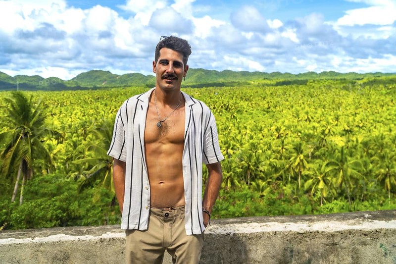 Young man posing in front of a large coconut plantation in siargao island, philippines, enjoying the tropical vibes