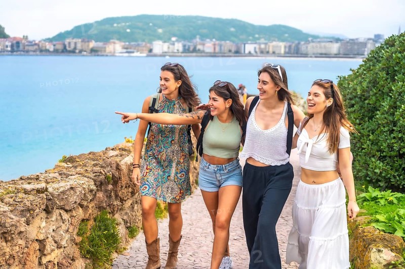 Happy young women walking a scenic mediterranean coastal path, laughing and pointing as they enjoy summer travel, friendship, and sightseeing together on vacation