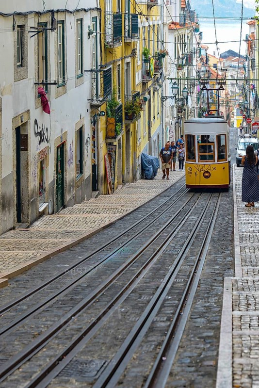 A yellow tram descends a steep, narrow alleyway full of charm in an urban setting, Lisbon, Portugal