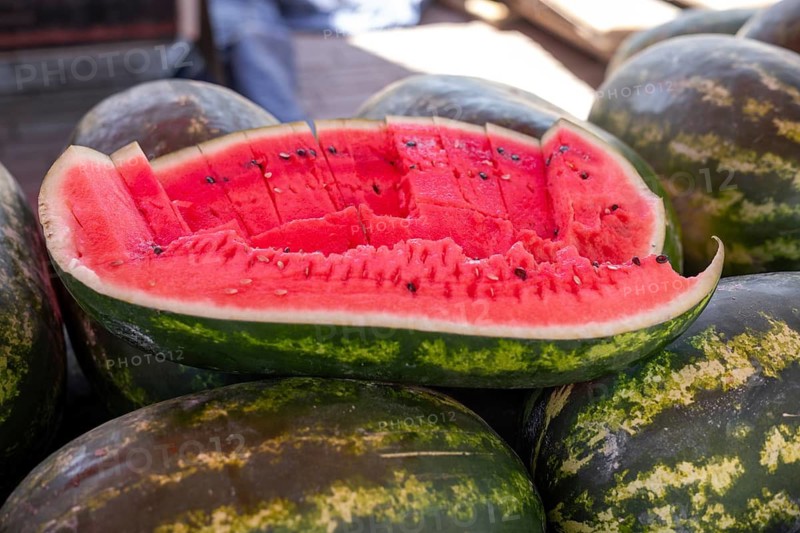 Sliced watermelon revealing juicy red flesh and seeds on a pile of whole ones
