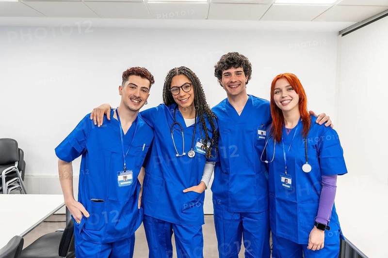 Diverse group of smiling medical students in blue scrubs with stethoscopes, arms around shoulders, standing together to show teamwork, friendship and collaborative learning in medicine