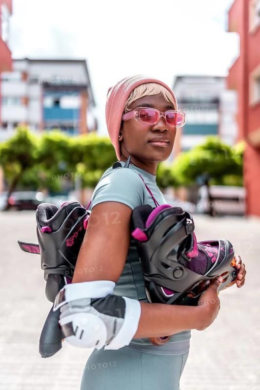 Vertical photo of a confident urban african woman with inline skates and protective gear for the elbows standing posing in the city