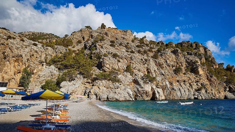 Rocky coastline with a beach full of parasols on a clear, sunny day, Ahata Beach, Ahata, East Coast, Karpathos, Dodecanese, Greek Islands, Greece