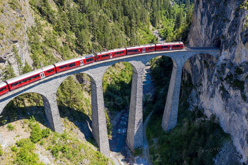 Drone shot of train passing the Landwasserviadukt near Filisur, red train of Bernina Express, Switzerland