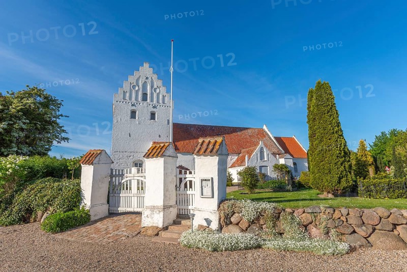 Whitewashed church in Dalby, side view, red roof, cemetery, stepped gable, entrance gate, stone wall made of erratic blocks, Fyn, North Funen, Denmark