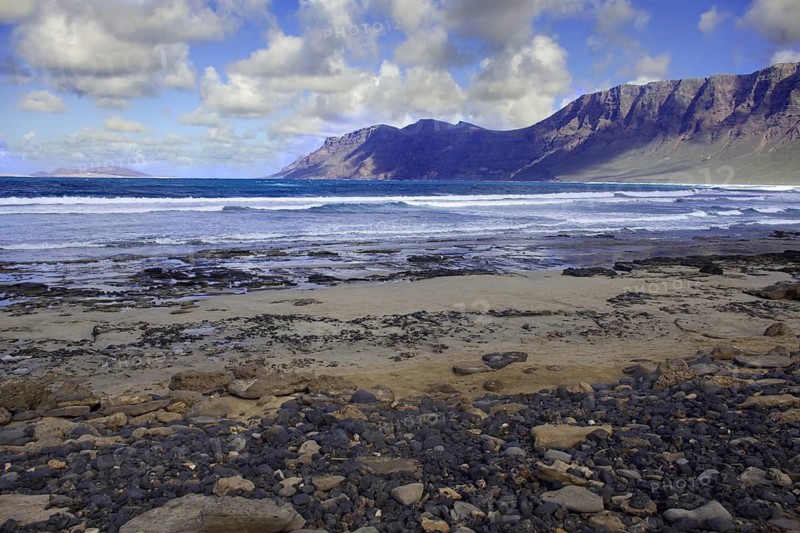 Coastal landscape with Famara cliffs (Risco de Famara) in the background and calm sea, Caleta de Famara