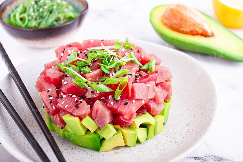 Fresh tuna tartare with avocado served on a marble table with soy sauce and seaweed salad