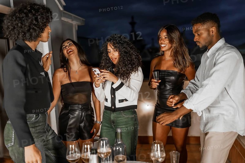 Multiracial chic friends using mobile phone during night party in a roof