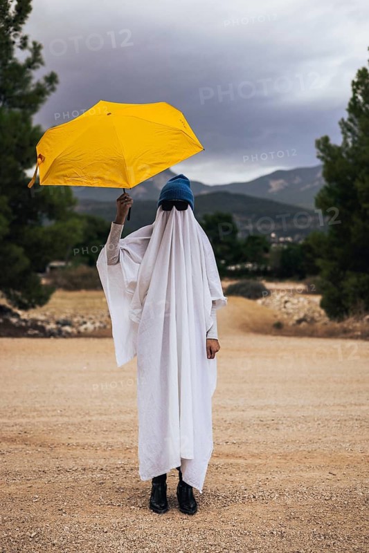 Playful ghost walking with a yellow umbrella outdoors during Halloween season. Creative homemade costume, autumn weather and spooky holiday atmosphere.