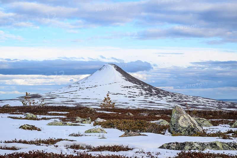 Snow-covered mountain under blue sky with clouds, surrounded by rocks and barren vegetation, evening mood at Städjan, Idre Fäll, Härjedalen, Sweden