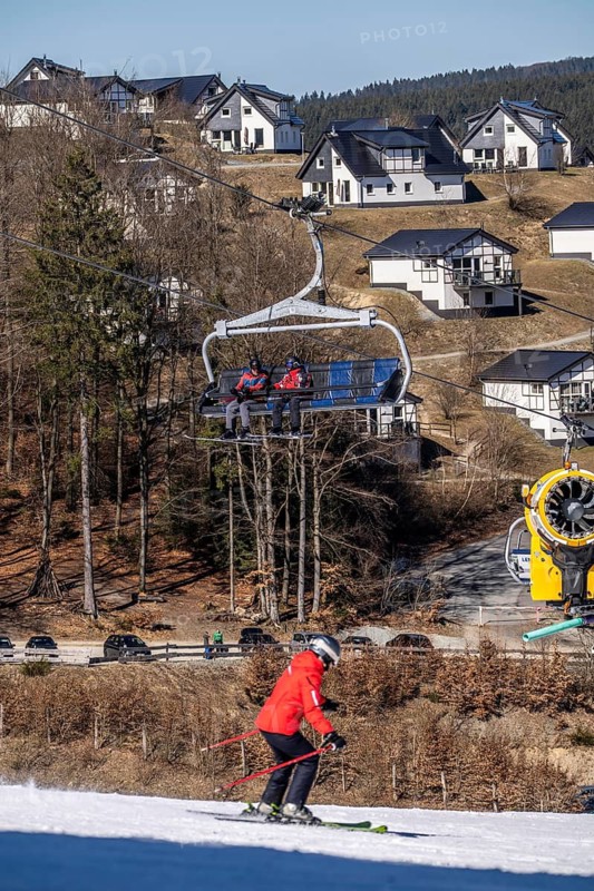 Winter sports area in the Sauerland, Winterberg ski lift carousel, artificial snow slopes, artificial snow from over 360 snow guns, Poppenberg ski area, 12 of 24 lifts are in operation in mid-March, the rest of the landscape is snow-free, in the background holiday homes at Landal Ferienpark Winterberg, North Rhine-Westphalia, Germany