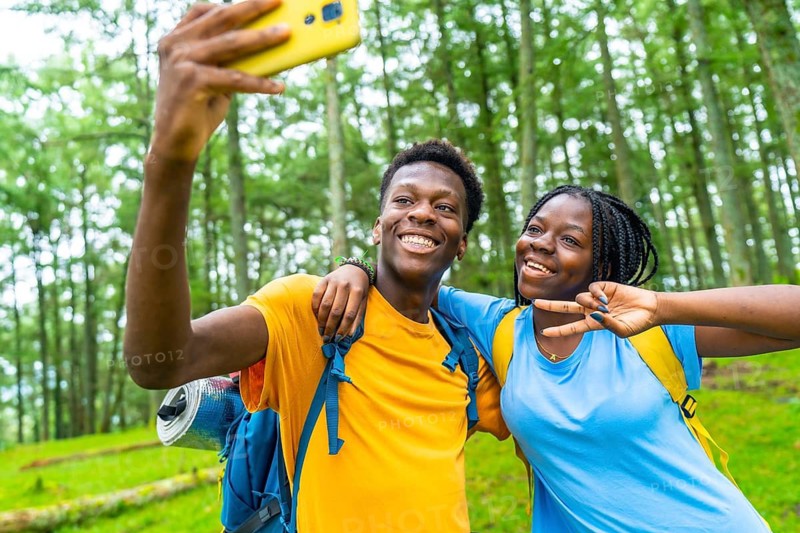 Happy young african friends gesturing success while taking selfie together in a green forest