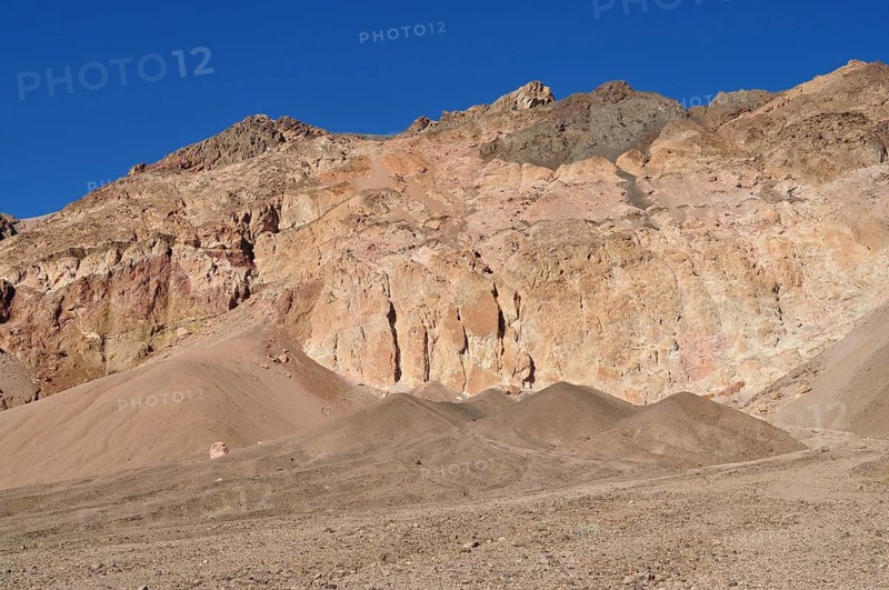 Erosion-shaped rock cliffs rise above a sandy desert landscape under clear skies, Artist Drive, Death Valley National Park, Mojave Desert, California, Nevada, USA