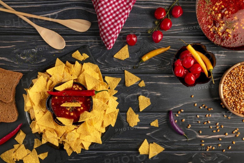 Tortilla chips in a bowl with chilli con carne, next to tomatoes, corn kernels and peppers