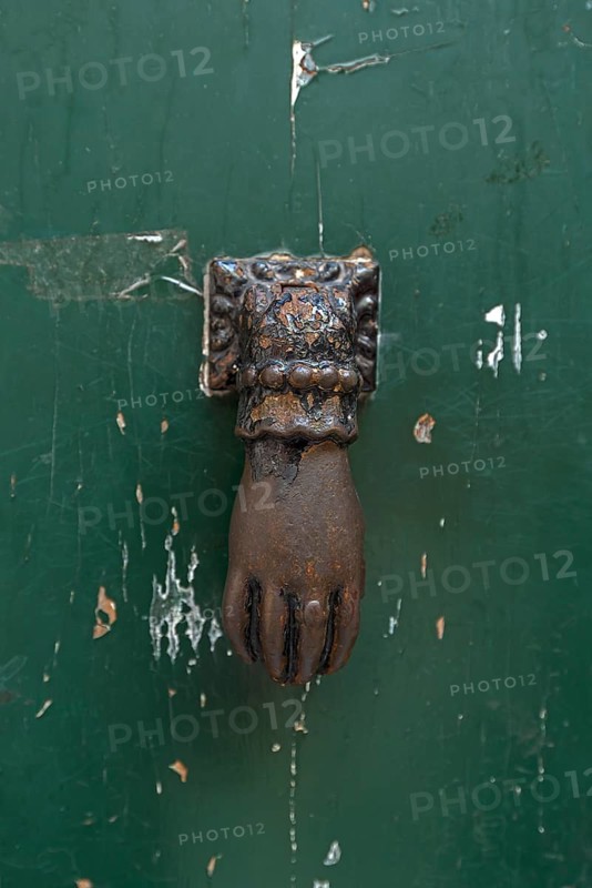 Hand as a door knocker on a front door in the historic centre, Genoa, Italy