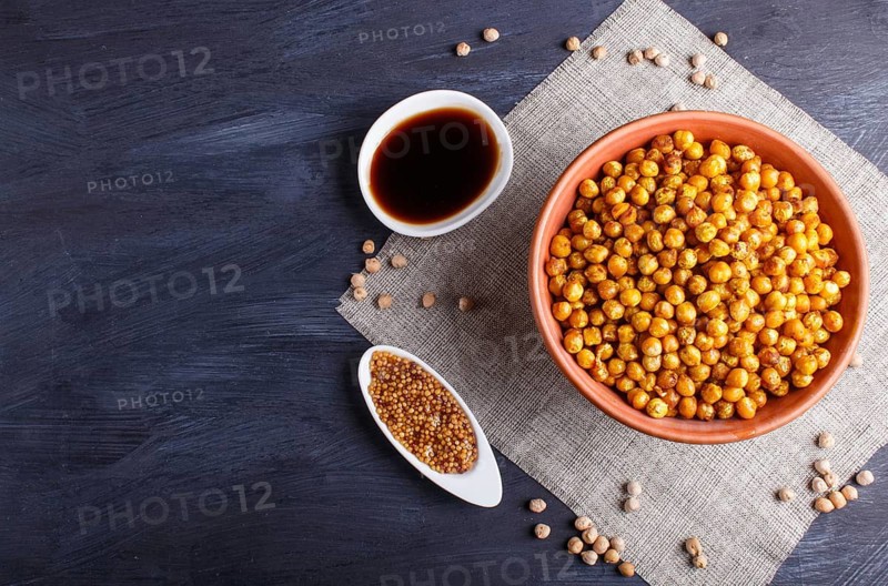 Fried chickpeas with spices in a clay plate on black wooden background, top view, copy space