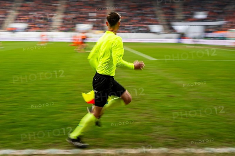 Assistant referee in a vibrant neon yellow kit running along the sideline during a professional soccer game with motion blur in Lubin, Poland