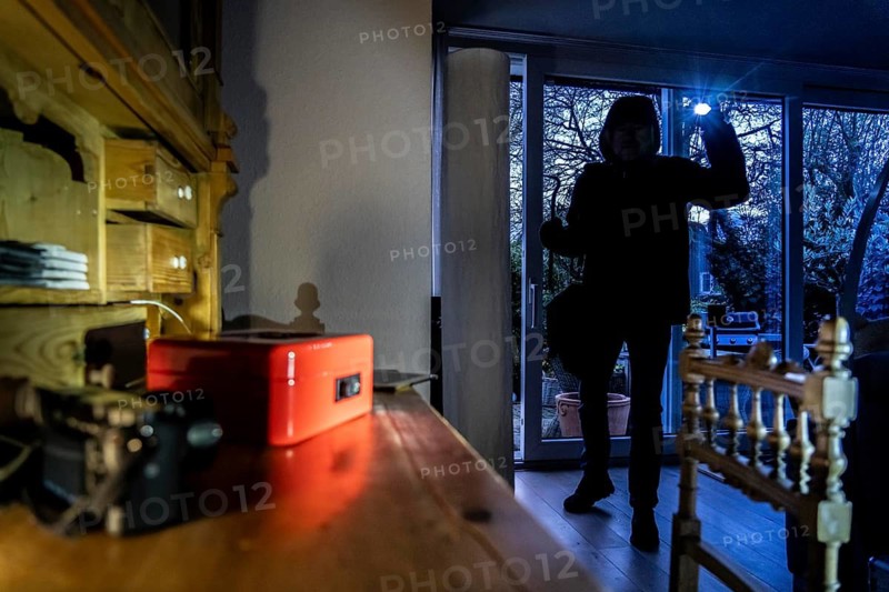 Symbolic image of a burglary, perpetrator has broken into a flat from the garden side and is looking for loot, cash box, valuables, money, technology