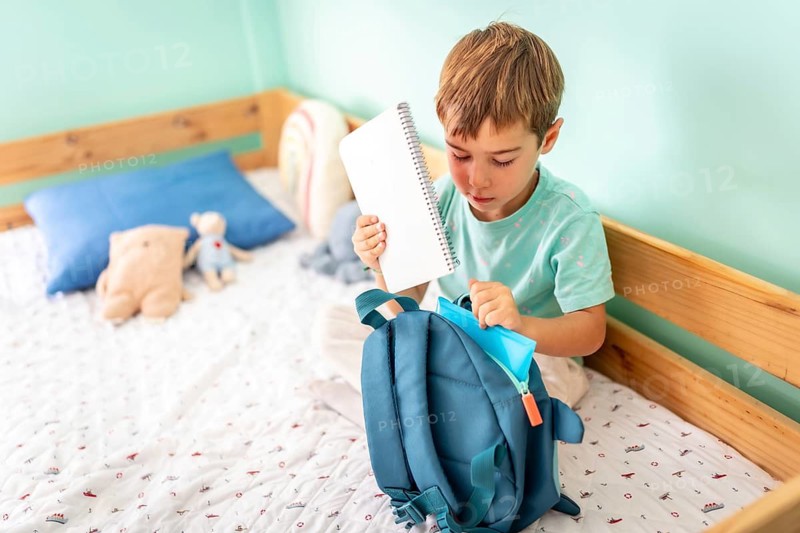 Schoolboy packing up his books in a school bag, and getting ready for another day of school in his room
