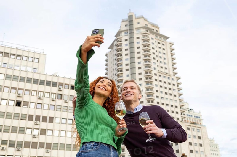 Friends is enjoying a rooftop party, capturing the moment with a selfie They smile and hold glasses against a backdrop of city buildings, embodying joy and celebration