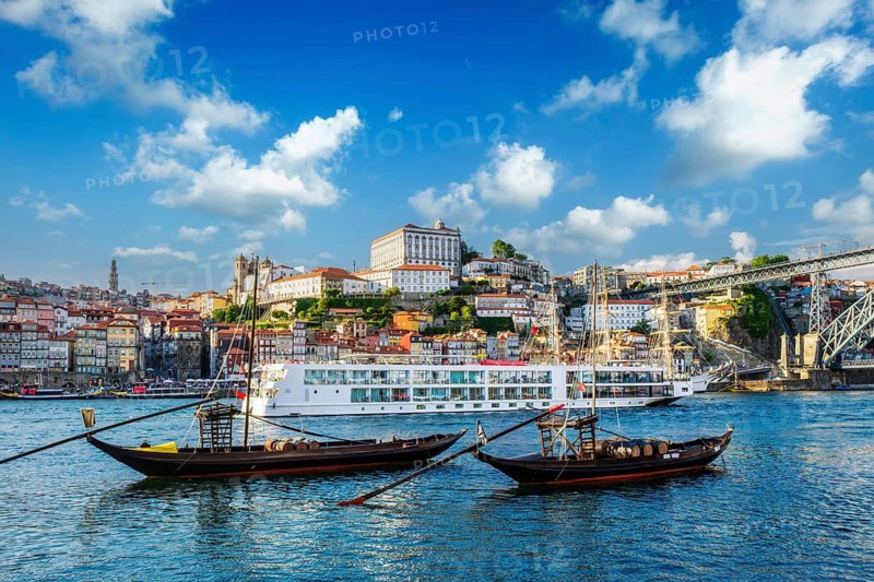 View of Porto city and Douro river with traditional boats with port wine barrels and sailing ship from famous tourist viewpoint Marginal de Gaia riverfront. Porto, Vila Nova de Gaia, Portugal