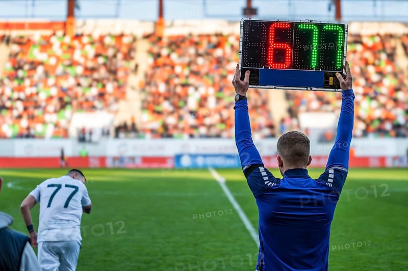 Rear view of a fourth official holding an electronic substitution board showing numbers 6 and 77 at a football stadium in Lubin, Poland