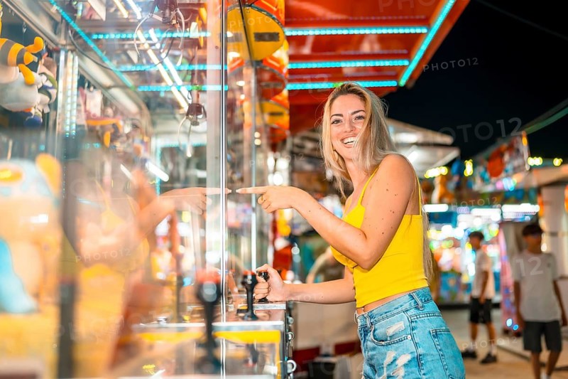 Happy caucasian blonde woman playing arcade games at fair at night