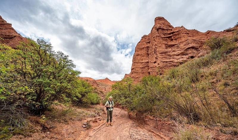 Mountaineer in a canyon with a dry stream bed, eroded mountain landscape with red sandstone rocks, Konorchek Canyon, Chuy, Kyrgyzstan