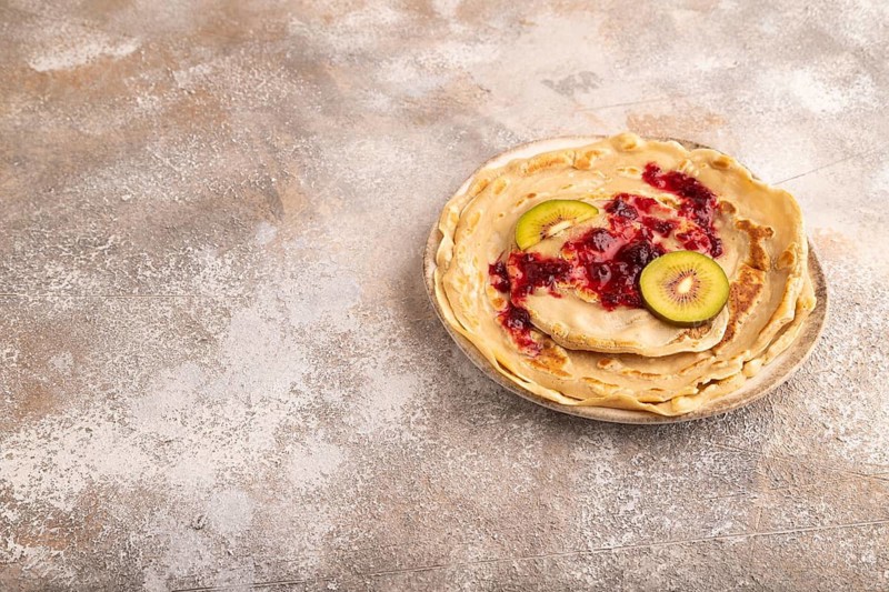 Stack of Plain Fried pancakes with jam and kiwi on brown concrete. side view, copy space