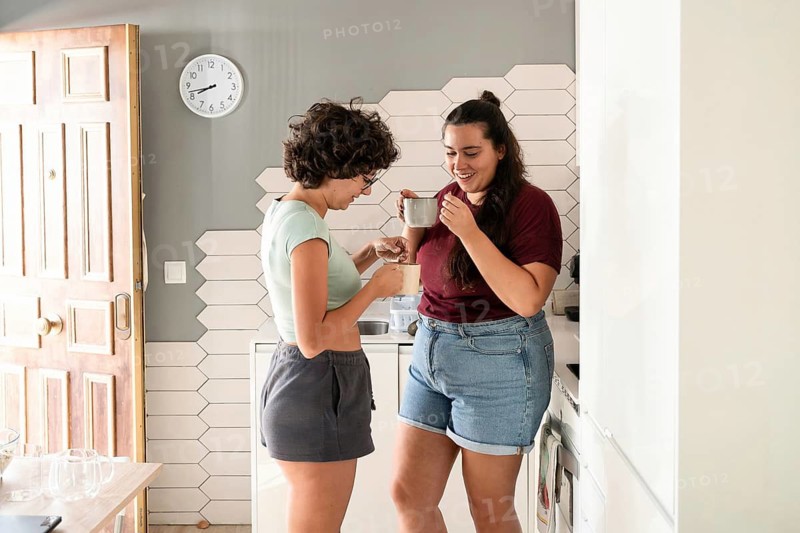 A loving lesbian couple enjoys a morning coffee together in their modern kitchen. They share smiles and warmth, creating a cozy and intimate atmosphere