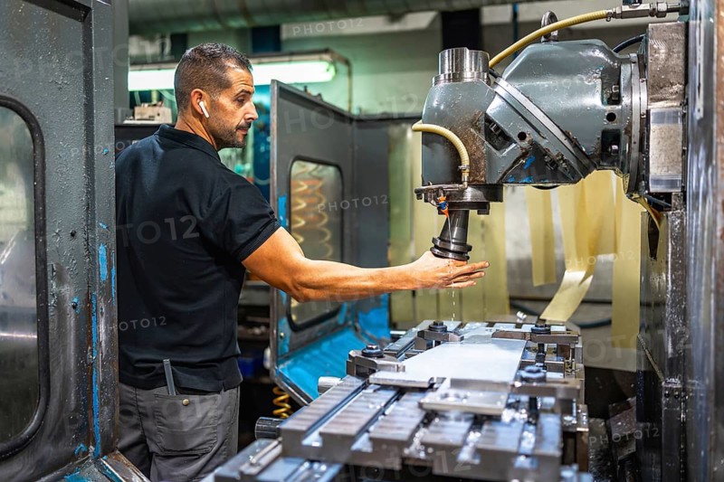 Three quarter length side view of a caucasian male worker using milling machine in a cnc factory