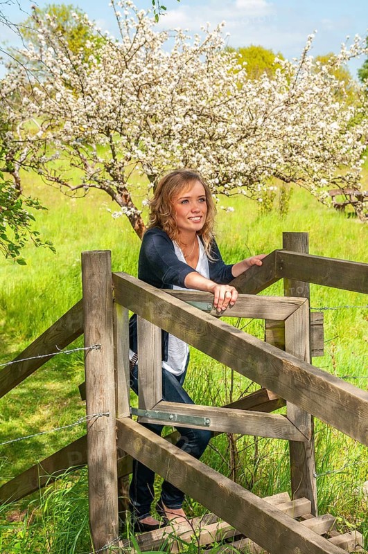 Young smiling woman opening a gate in a fence and with a blooming apple tree in the background in Brösarp, Simrishamn municipality, Skjåne county, Sweden, Scandinavia