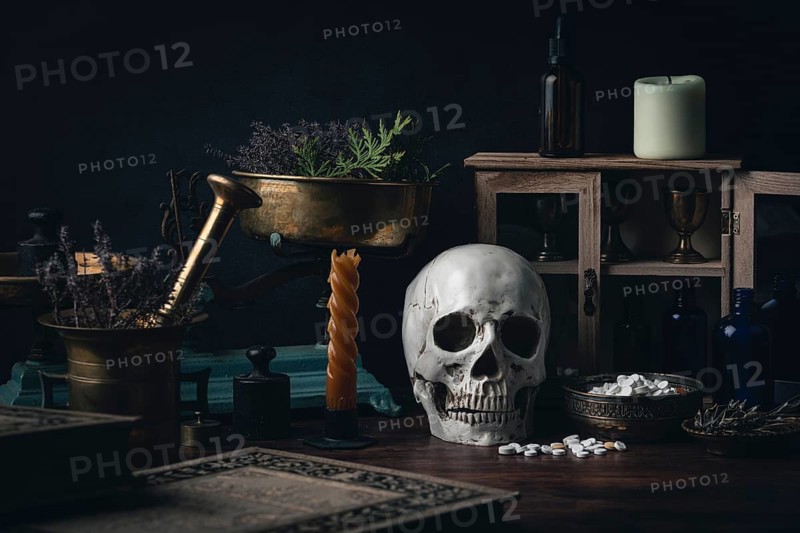 Dark alchemical setting with skulls, candles, mortars, herbs and pills