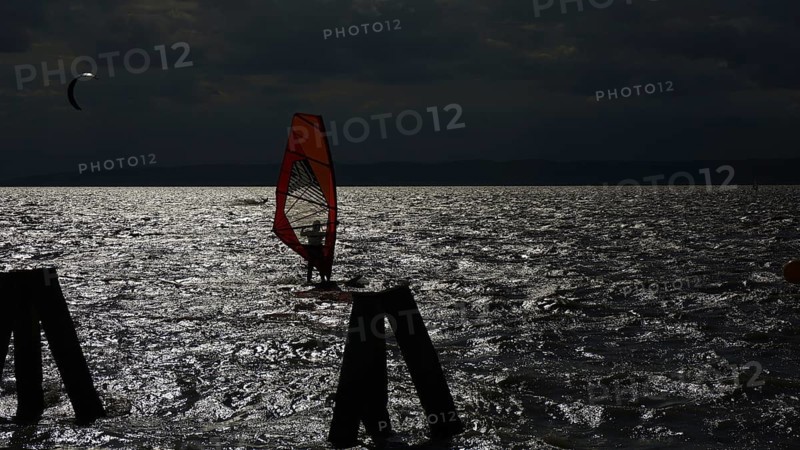 A surfer silhouette in moonlight on a dark, wavy lake, Lake Neusiedl, Austria