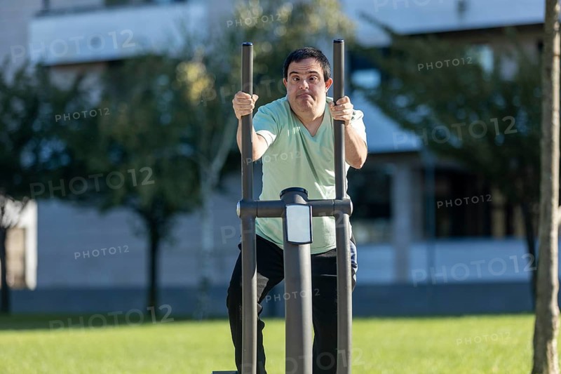 Man with an intellectual disability uses outdoor fitness equipment in a park. His focused expression highlights determination and the importance of physical activity for well-being and inclusion
