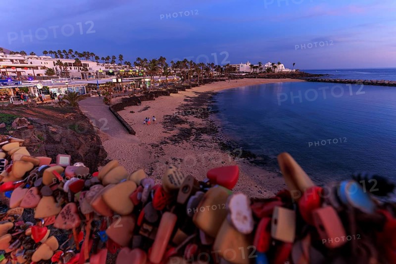 Lanzarote, Canary Islands, Spain, Europe, Playa Blanca, Love Castles, A stretch of coast with love locks in the foreground and a city in the background at dusk