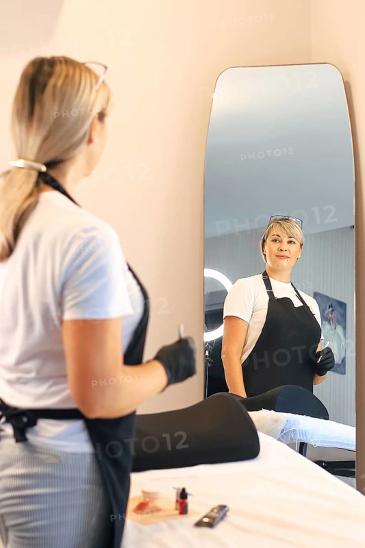 A woman in an apron looks at her reflection in a large mirror, creating a calm and professional atmosphere