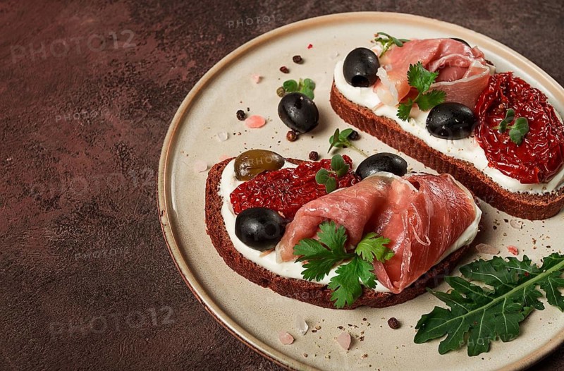 Sandwiches with cheese and prosciutto, dried tomatoes and olives, breakfast on a plate