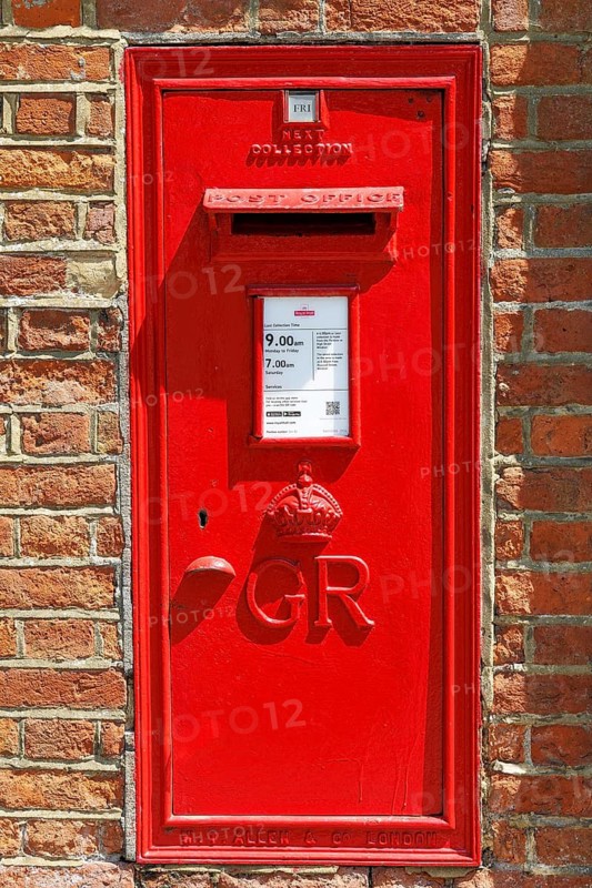 A red post box in Chapter Mews bears the royal cypher of King George V, who reigned from 1910 to 1936, set within a plain brick wall as a small reminder of the interwar postal infrastructure serving the castle precincts, Windsor, England, United Kingdom