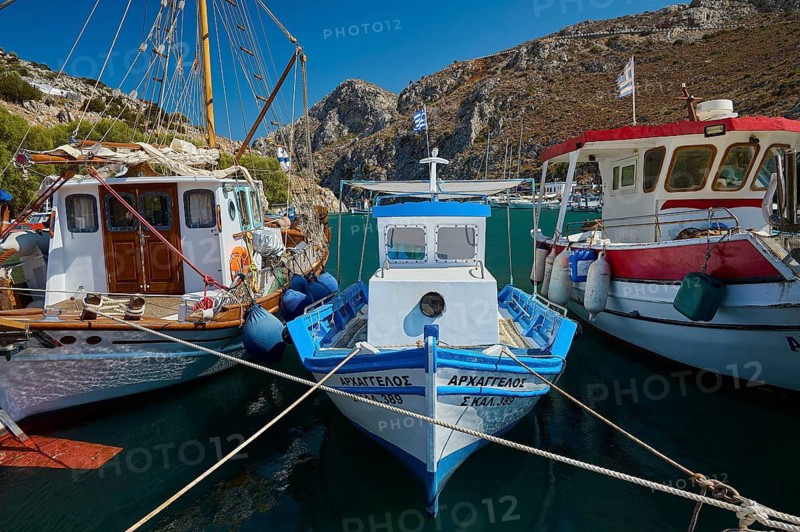 Colourful boats are lying in the harbor against a rocky coastal landscape under a blue sky, Rina, harbour, Vathi, Vathys, Kalymnos, Dodecanese, Greek Islands, Greece